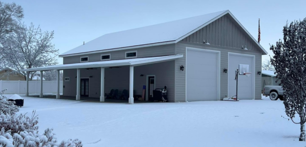 A snow-covered garage with a charming porch, showcasing single-story barndominium design for easy living and accessibility.