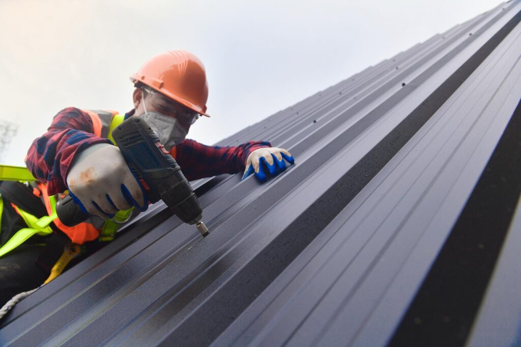 close up drill Roofer worker in protective uniform wear and gloves,Roofing tools,installing new roofs under construction,Electric drill used on new roofs with metal sheet.